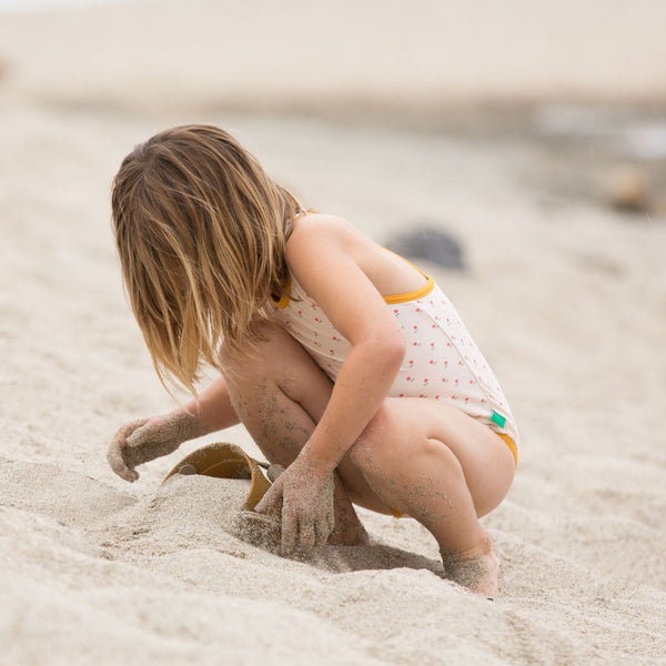 Bambina gioca in spiaggia indossa costume da bagno intero panna con rose