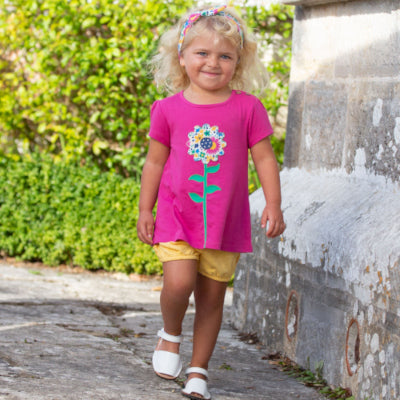 bambina bionda cammina indossa maglietta viola con fiore colorato e pantaloncini gialli con margherite