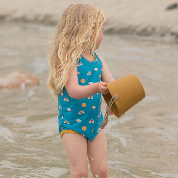 Bambina in spiaggia indossa costume da bagno intero azzurro con arcobaleno