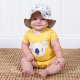 neonato seduto su un tappeto indossa un bosy giallo in cotone con koala e cappellino