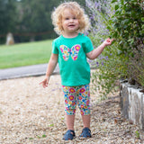 bambina bionda con i riccioli indossa maglietta verde con farfalla e leggings a fiori colorati