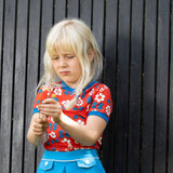 bambina bionda gioca con un fiore indossa maglietta a maniche corte rossa con fiori bianchi e blu