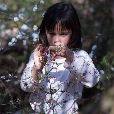 bambina guarda un fiore con camicetta bianca e fantasia di uccellini