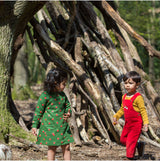 due bambini in un bosco indossano vestito verde con mele rosse maniche lunghe e tuta intera rossa con maglione giallo