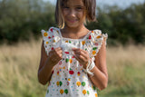 bambina sorridente indossa un abito color panna con alberi di mele e tiene tra le dita un fiocco di cotone.