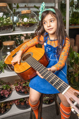 bambina seduta con in mano una chitarra indossa maglietta arancione cpon fiorellini e abito blu