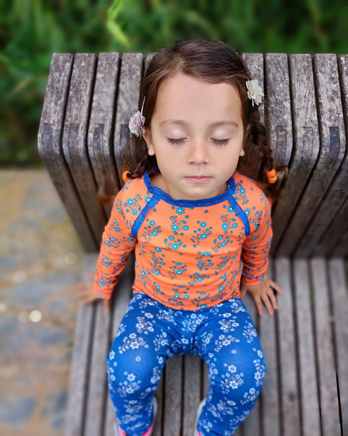 bambina che dorme indossa maglietta a maniche lunghe arancione con fiorellini e leggings blu con fiorellini