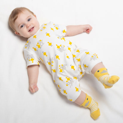 neonato disteso su uno sfondo bianco con pagliaccetto bianco con anatre gialle disegnate e calzini gialli