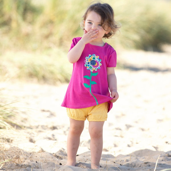 Bambina in spiaggia indossa maglietta viola con fiore colorato e pantaloncini gialli con margherite