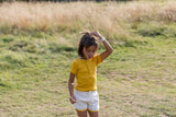 bambina in un campo di grano indossa una maglietta gialla e pantaloncini color crema con bordo a contrasto giallo