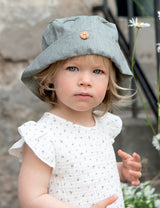 Bambina indossa cappellino verde chiaro e camicetta con maniche ad aletta bianca con fiorellini verde chiaro