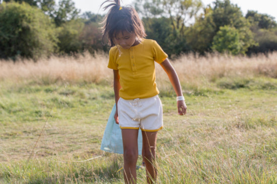 bambina in un campo indossa maglietta a coste gialla e poantaloncini a coste crema con bordo giallo