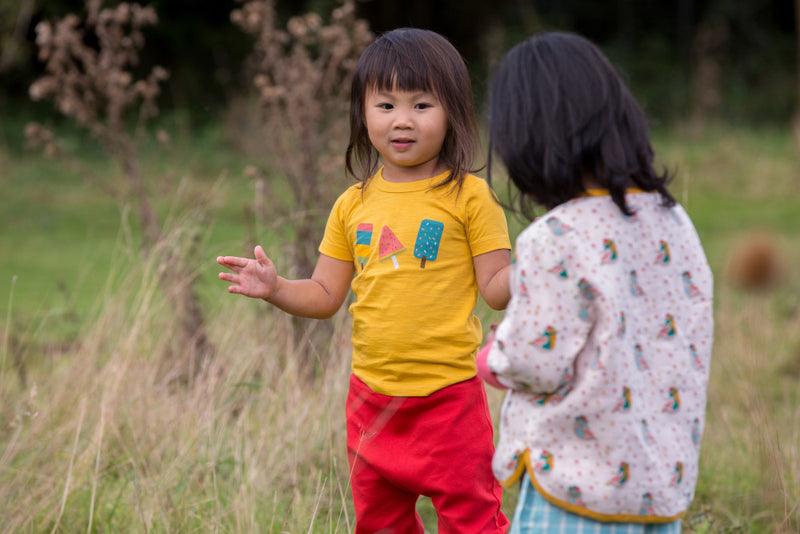 bambina in un campo indossa maglietta gialla con stampa colorata mNICHE CORTE IN COTONE PANTALONI ROSSI