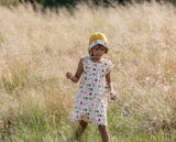 bambina cammina in un prato e indossa cappellino giallo e panna abiro panna con mele