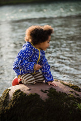 Bambino su una roccia indossa giacca impermeabile azzurra con fulmini e leggings a righe panna e bronzo