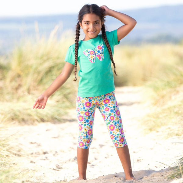bambina in spiaggia indossa maglietta a maniche corte verde con farfalla e leggings a fiori colorati
