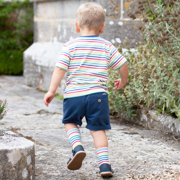 bambino di schiena che corre indossa maglietta a righe colorata a maniche corte e pantaloncini blu navy