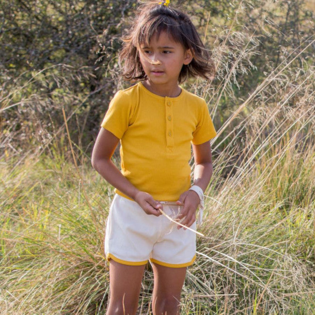 bmbina in un campo indossa maglietta a coste gialla e pantaloncini a coste crema con bordo giallo